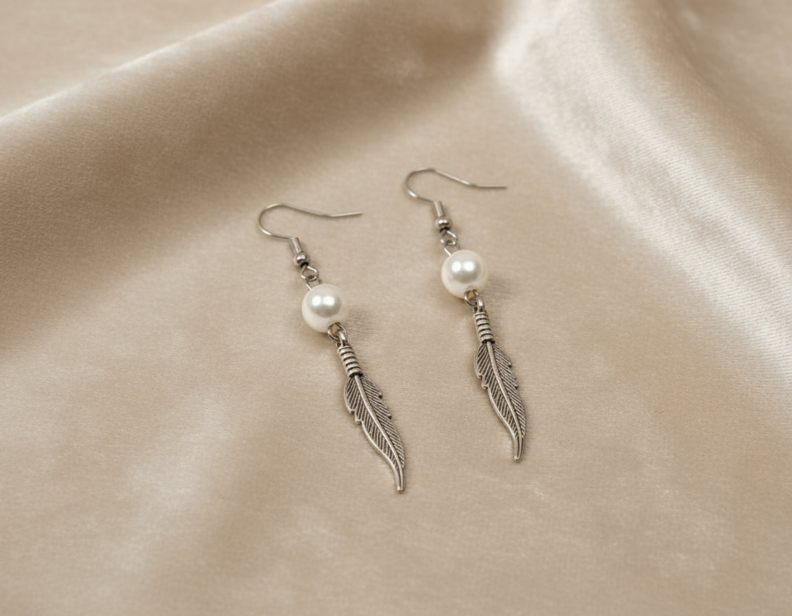 Silver feather earrings with pearls on a beige fabric background