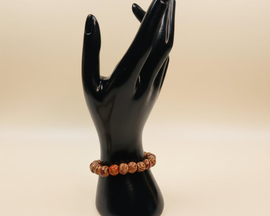 Black mannequin hand holding a brown beaded bracelet on a beige background
