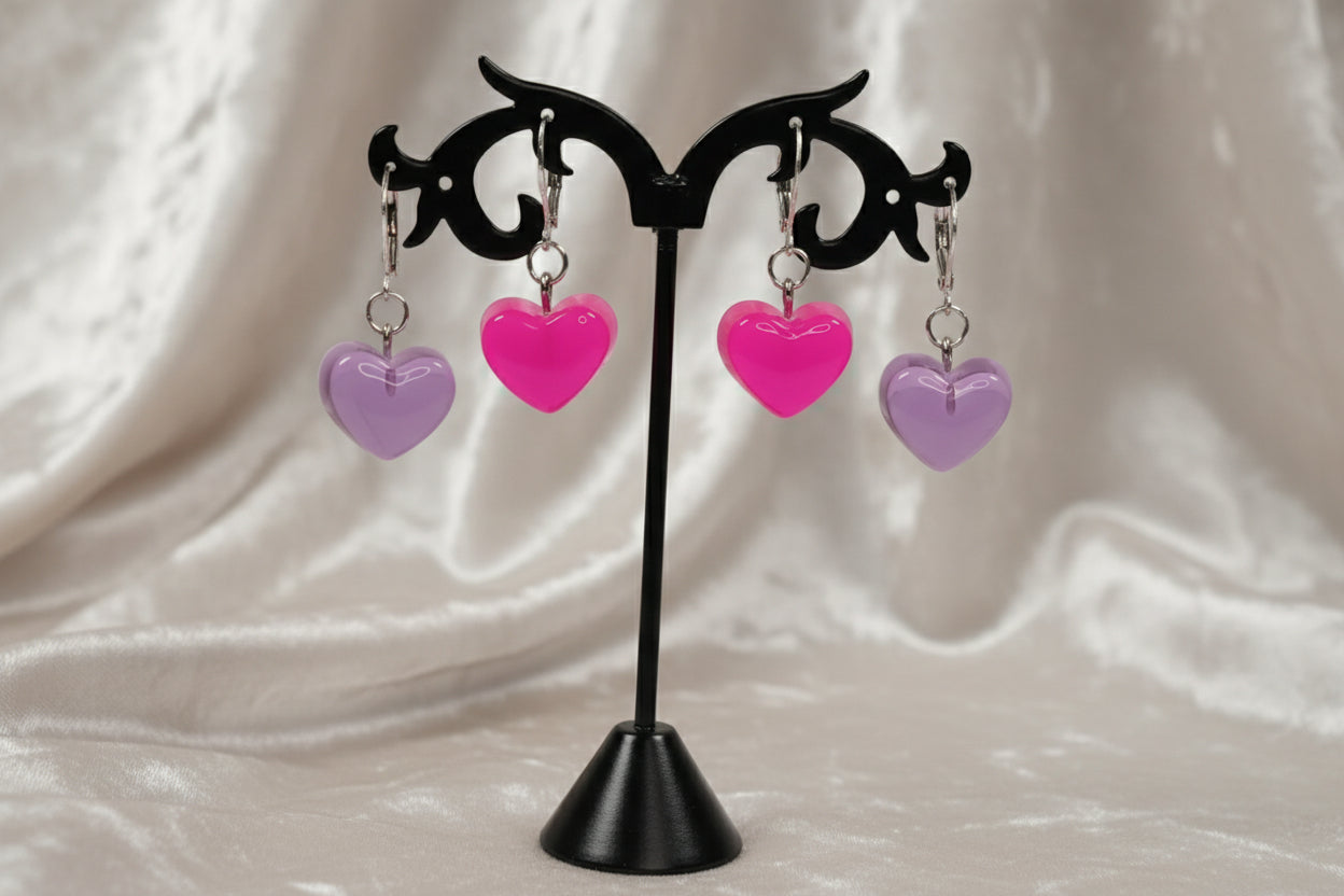 Heart-shaped earrings on a black stand against a white background