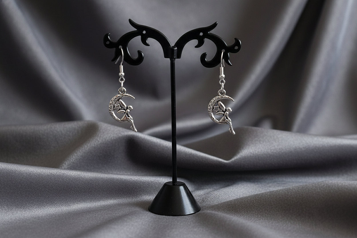 A pair of silver-plated zinc alloy dangling earrings with intricate fairy designs, displayed on a black earring stand.