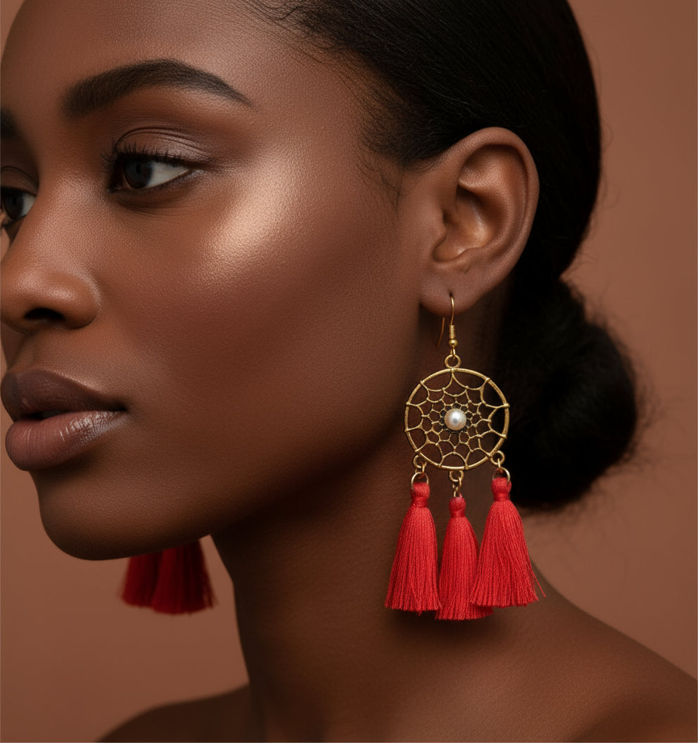 Close-up of a woman wearing a gold earring with red tassels against a brown background