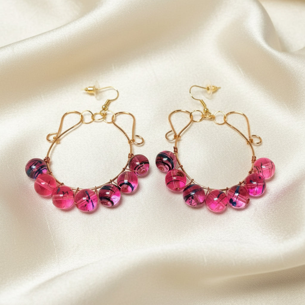 Gold copper wire hoop earrings with glass beads lying on a soft cloth