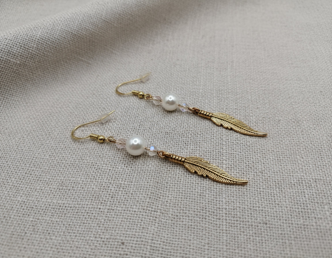 Gold dream catcher feather earrings with silver beads lying on a soft cloth