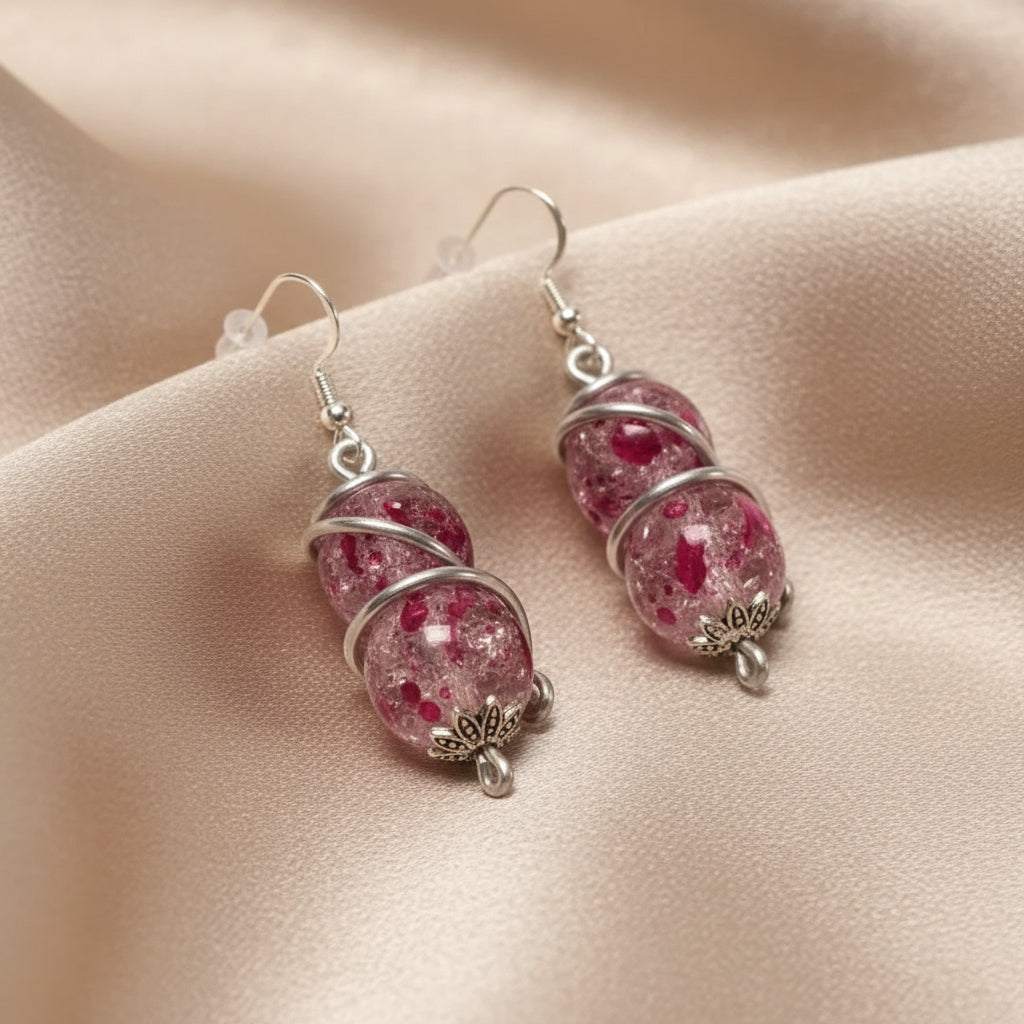 Pink double spiral wrapped earrings with glass beads lying on a soft cloth