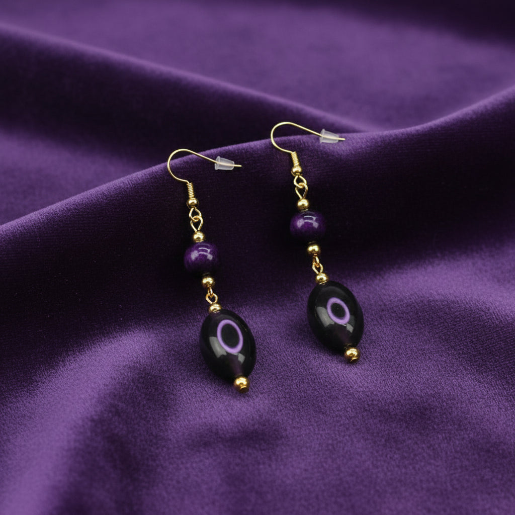 Purple dangling earrings with round and oval beads lying on a soft cloth