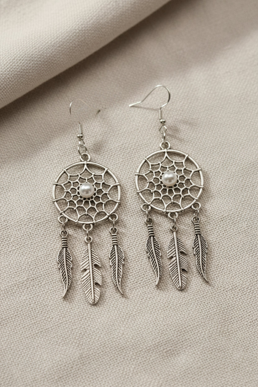 Silver dream catcher earrings with ivory pearl beads lying on a soft cloth