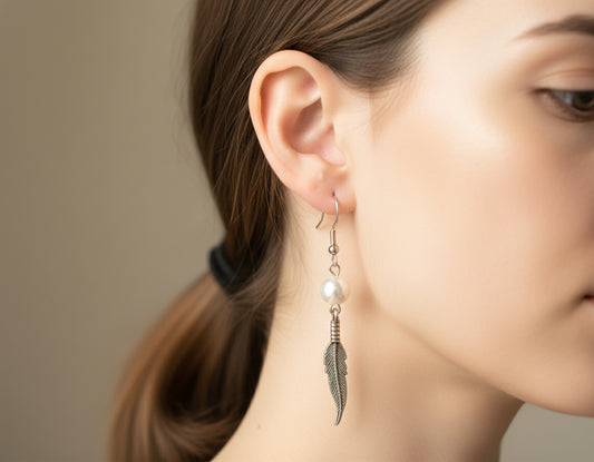 Close-up of a woman wearing a feather-shaped earring with a pearl accent.