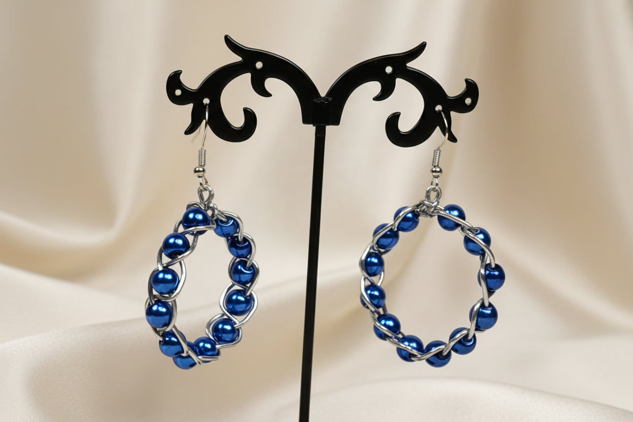 Pair of blue beaded hoop earrings on a black earring stand against a white background