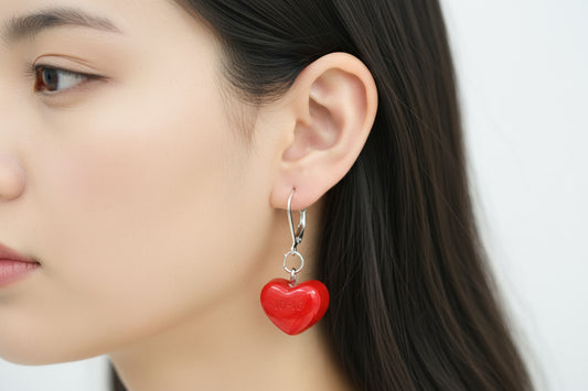 Close-up of a person wearing a red heart-shaped earring against a neutral background