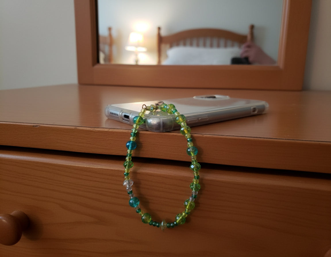Phone with green and blue beaded strap on a wooden surface