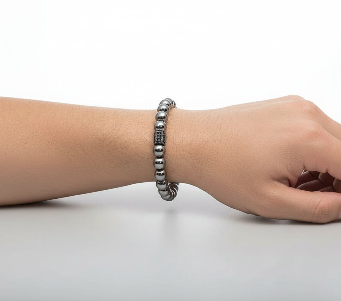 Hand wearing a silver beaded bracelet on a plain background