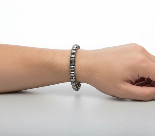Hand wearing a silver beaded bracelet on a plain background