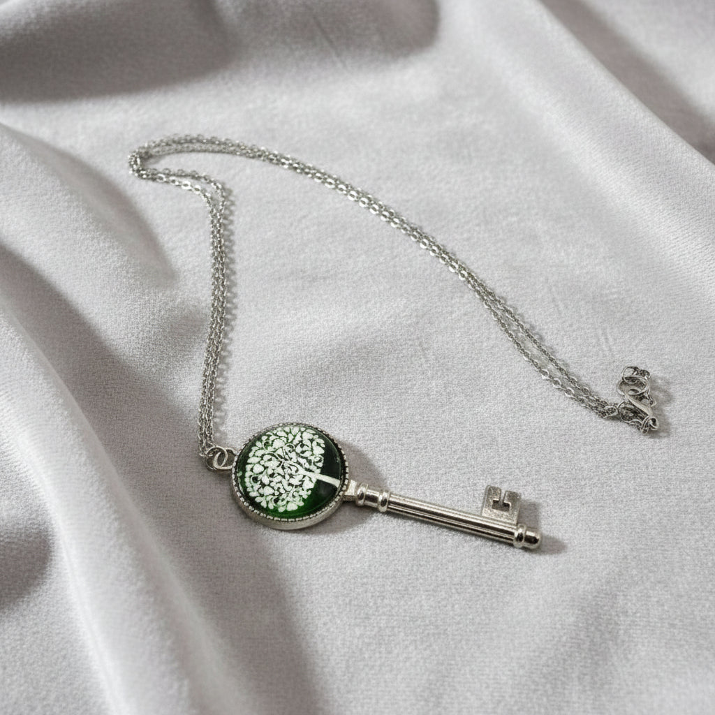 Silver key-shaped pendant with green accents on a white fabric background