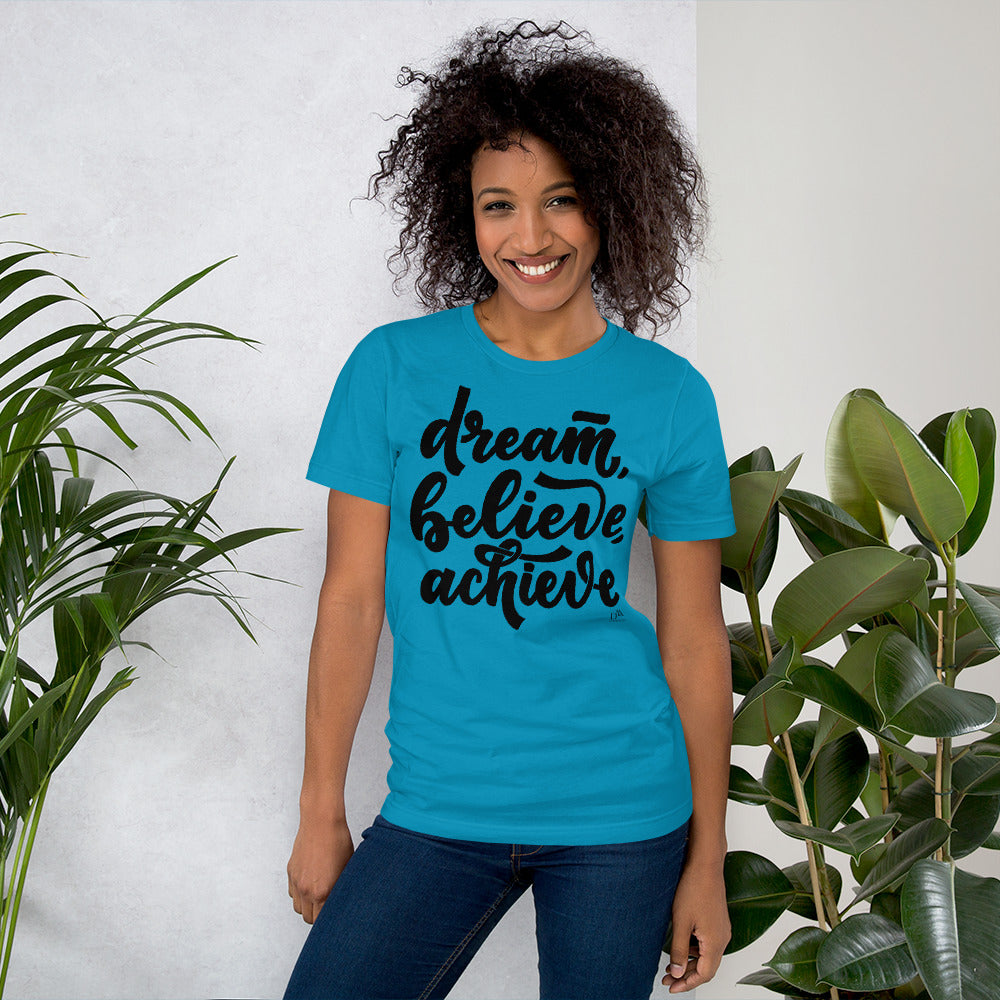 Woman wearing a blue t-shirt with 'dream, believe, achieve' text standing between two plants.