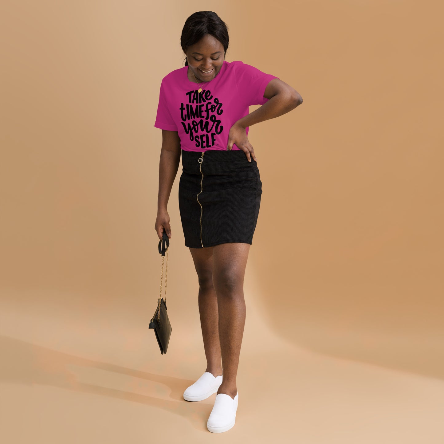 Woman wearing a pink t-shirt with text and black skirt on a beige background