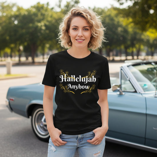 Woman wearing a black t-shirt with 'Hallelujah Anyhow' text, standing in front of a vintage car.