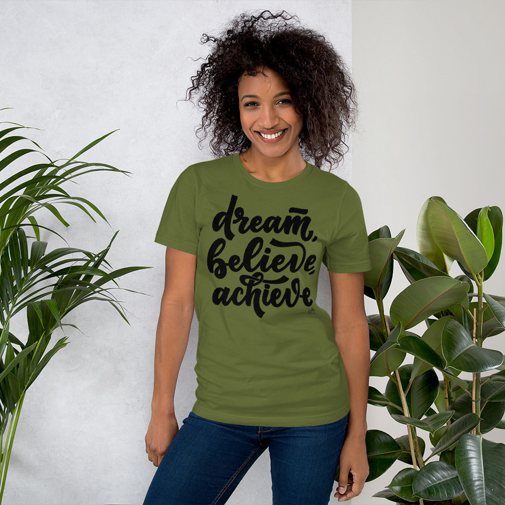 Woman wearing a green t-shirt with 'dream, believe, achieve' text, standing between two plants.