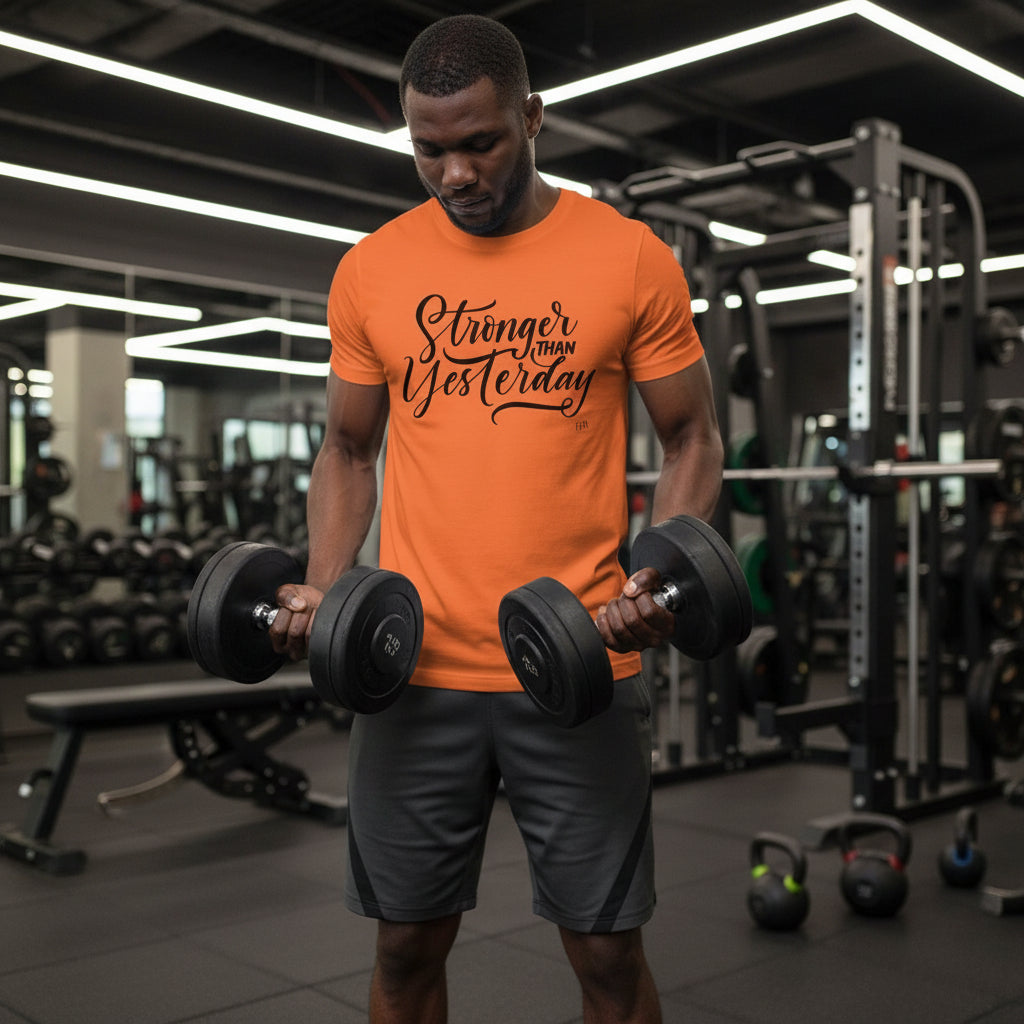 Man lifting dumbbells in a gym wearing an orange t-shirt with motivational text.