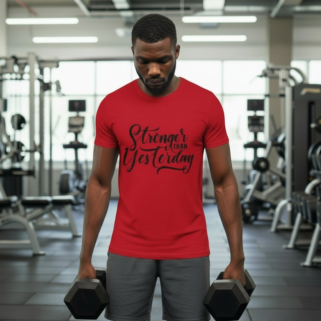 Man in a gym wearing a red t-shirt with motivational text, holding dumbbells.