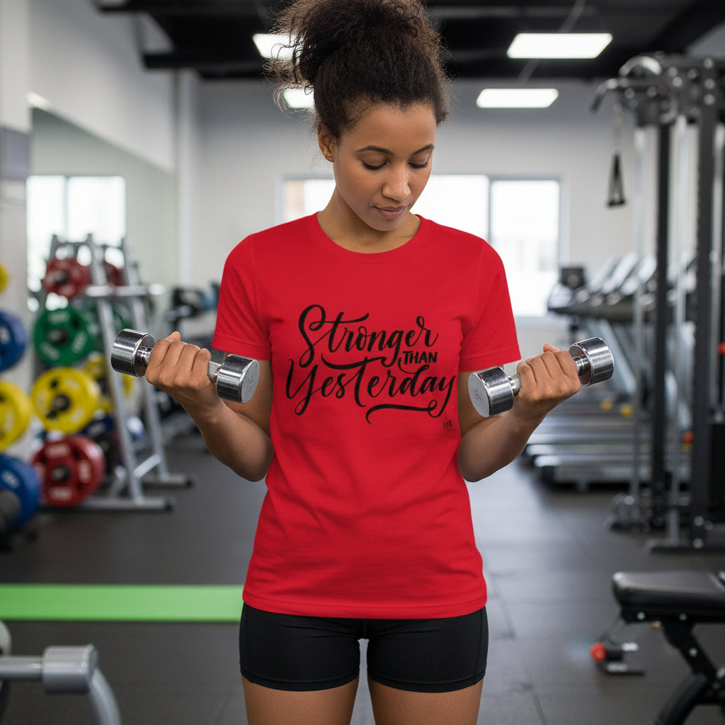 Woman in a gym wearing a red t-shirt with 'Stronger Than Yesterday' text, holding dumbbells.