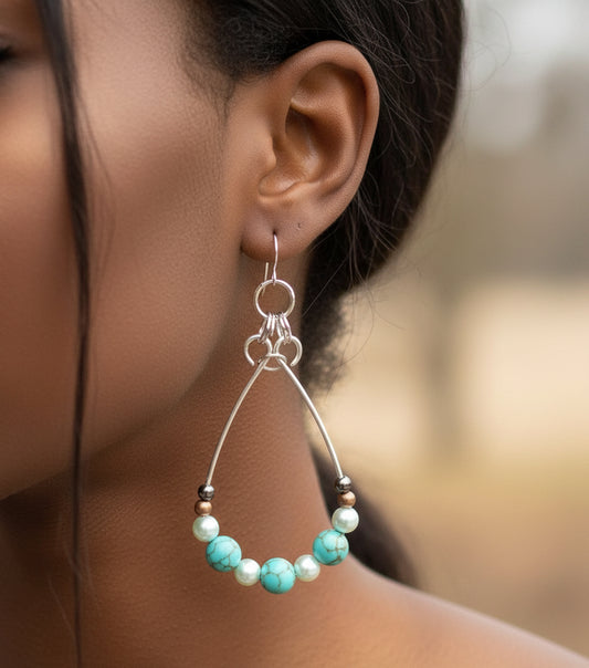 A woman wearing handmade Howlite teardrop earrings with turquoise wire and natural stones